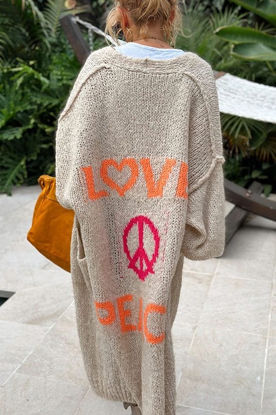 Strikket cardigan med LOVE og PEACE-design i naturmiljø og sennepsgul håndveske.