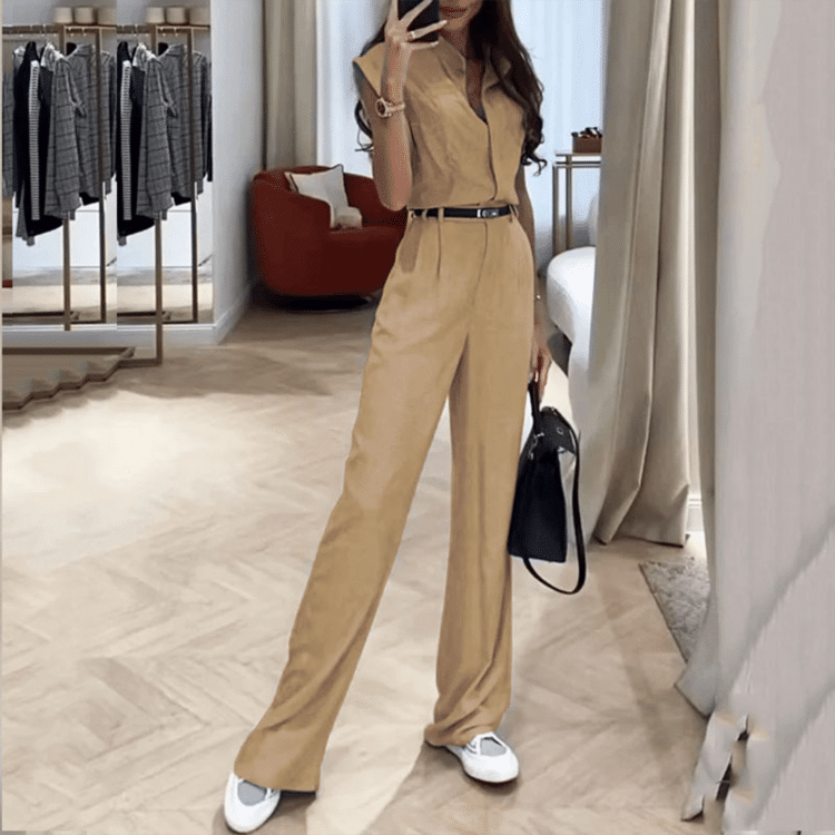 Trendy person i chic beige jumpsuit, hvite joggesko og svart håndveske i luksuriøst rom.