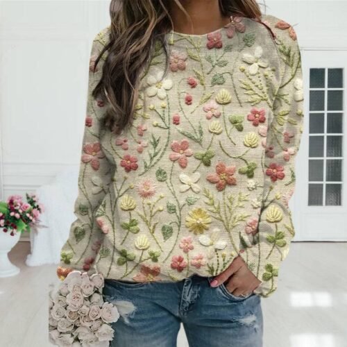 Person i blå blomstersweater og jeans holder matchende bukett i lyst rom.