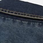 Nærbilde av blå denim tekstur med tydelig twill-vev og pent utførte gule sømmer.