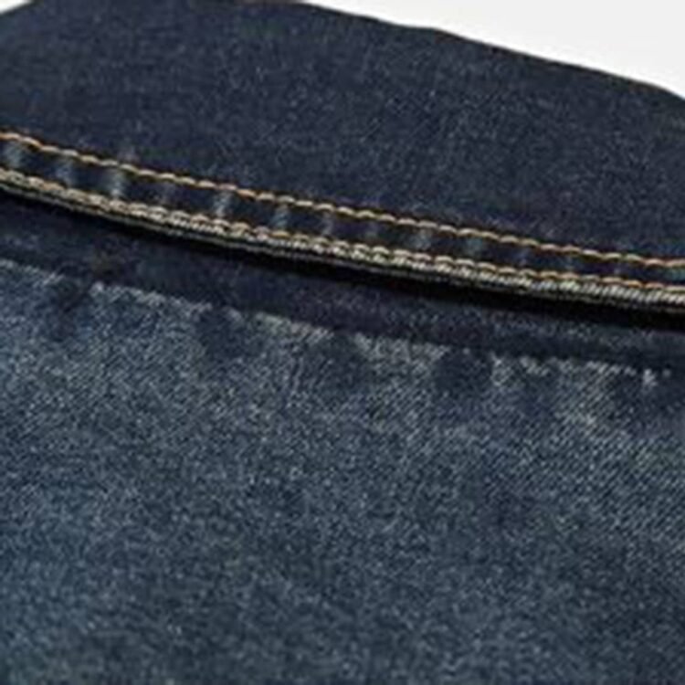 Nærbilde av blå denim tekstur med tydelig twill-vev og pent utførte gule sømmer.