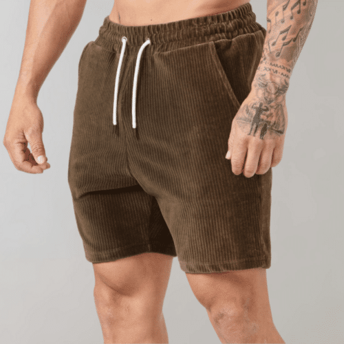 Person med tatoveringer iført brun corduroy shorts i nøytral bakgrunn.