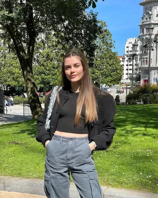 Stilig kvinne smiler i urban park med gråe cargobukser og lys håndveske.