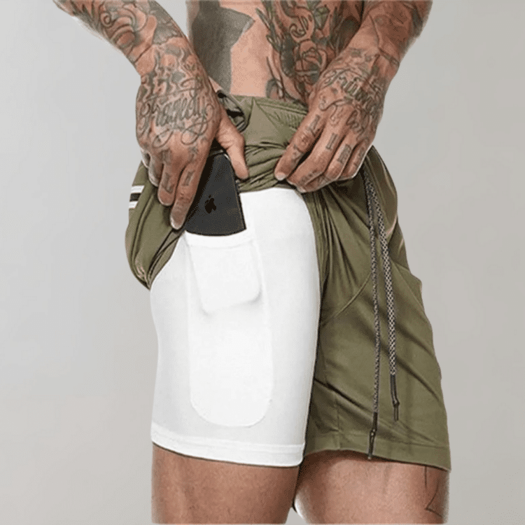 Grønne shorts med lomme og tatoverte hender justerer mobiltelefon i hvite compression shorts.