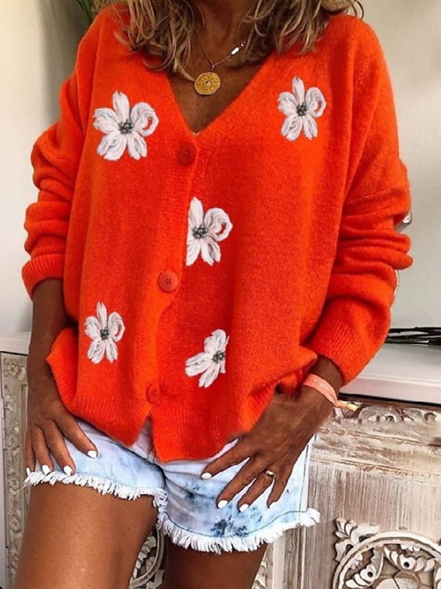 Orange cardigan med hvite blomster, blå denim shorts og gull halskjede på rustikt møbel.