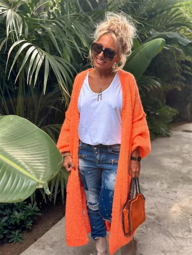 Stilig kvinne i orange cardigan og jeans i frodig hage, avslappet og elegant uttrykk.