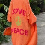 Person går i orange cardigan med LOVE og PEACE budskap i grønn hage.