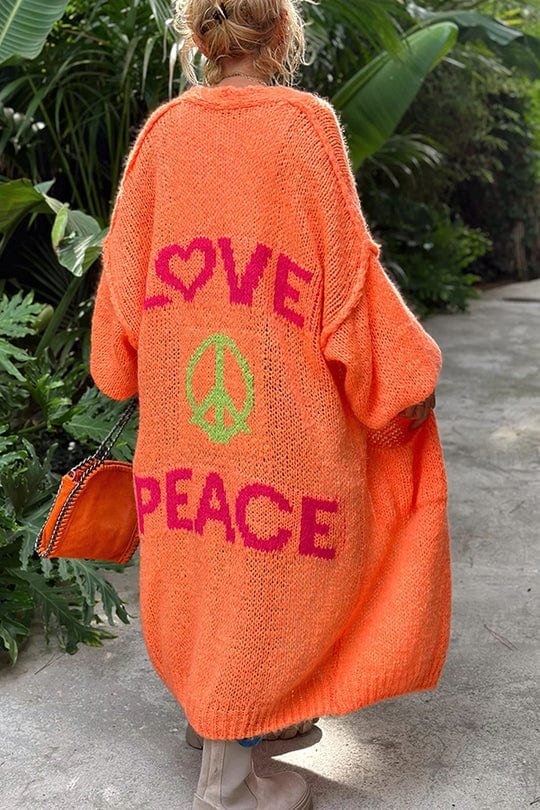 Person går i orange cardigan med LOVE og PEACE budskap i grønn hage.