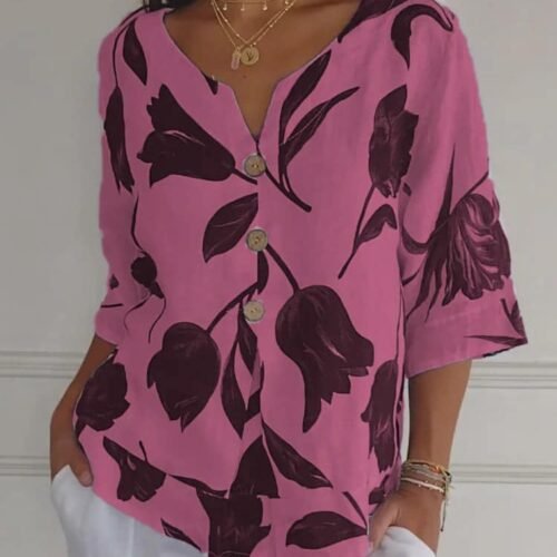 Stilig rosa blomsterbluse med hvit bukse, elegant antrekk med gullaccessories.