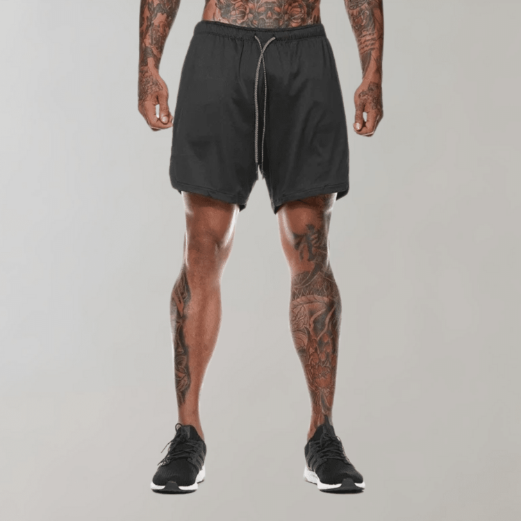 Svart athleisure shorts med tatoverte ben og moderne joggesko - stil og kunst.