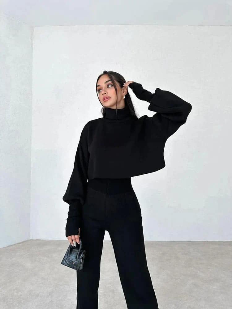 Moderne chic stil: Svart turtleneck, bukser og håndveske i lyst rom.